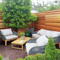 slatted fence panels made from cedar in a garden with seating. the fencing surrounds the area and planting makes the scence look very relaxed.