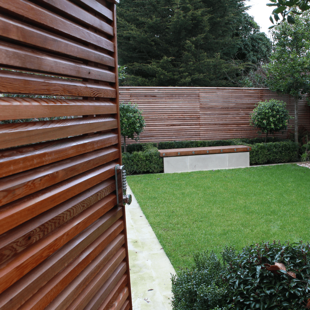 A double sided cedar gate half open, revealing the inside of a contemporary fenced garden.