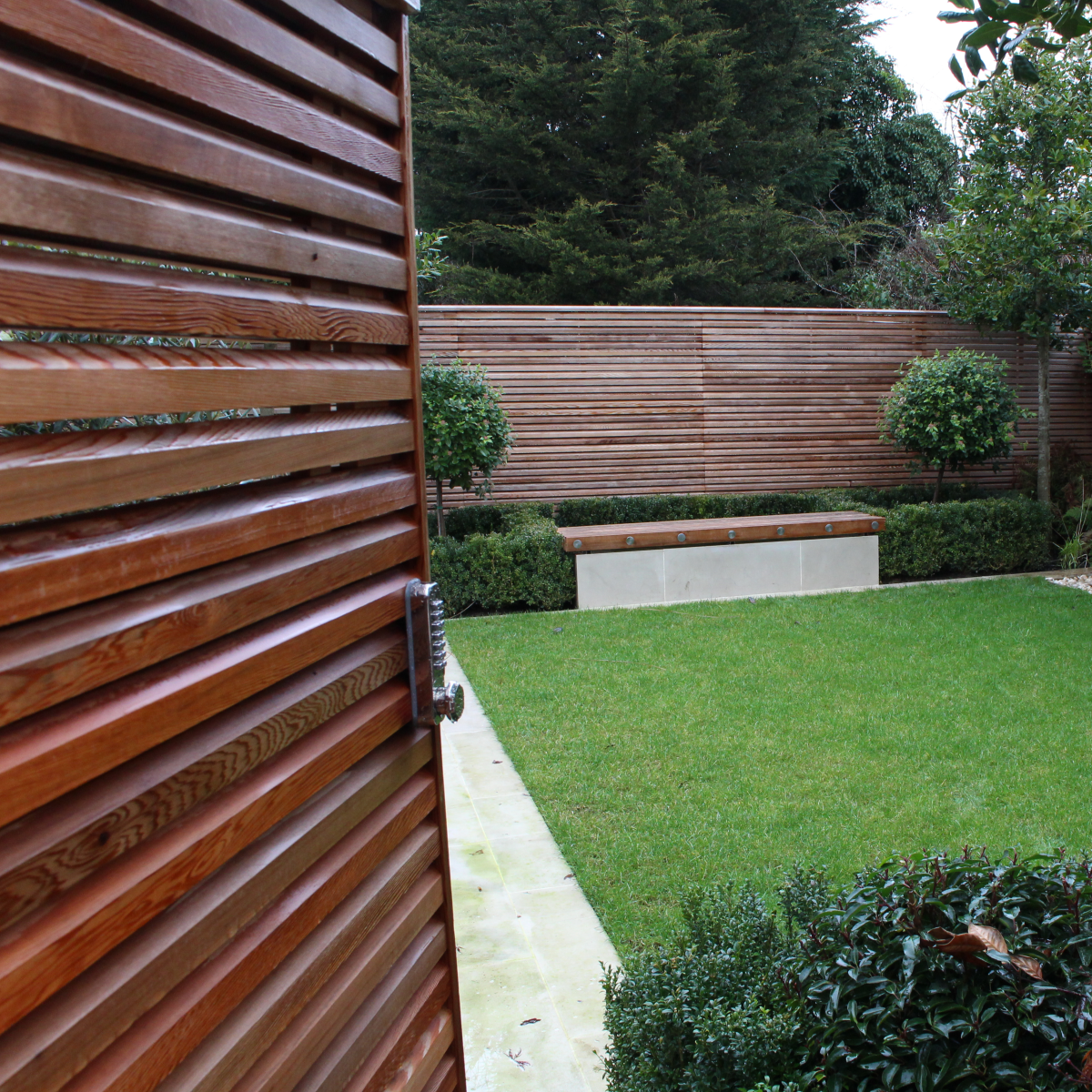 A double sided cedar gate half open, revealing the inside of a contemporary garden.