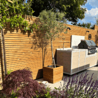 Contemporary slatted fence panel next to a garden barbeque and patio.
