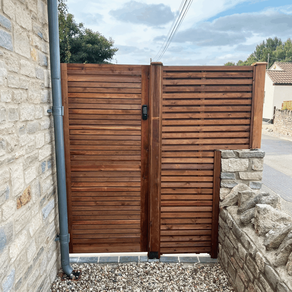 double slatted gate made from Scandinavian Redwood. attached to a stone house with a double sided venetian fence panel alongside.
